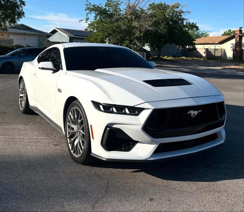 White Ford Mustang parked on a street with trees and houses in the background