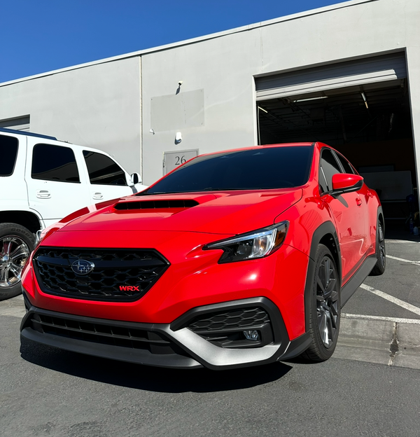 Red car parked in front of a white building with a clear blue sky.