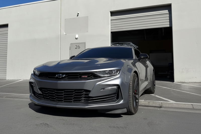 Gray Chevrolet car parked in front of a building with a white SUV in the background.