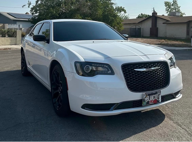 White Chrysler car parked on a street with houses and trees in the background